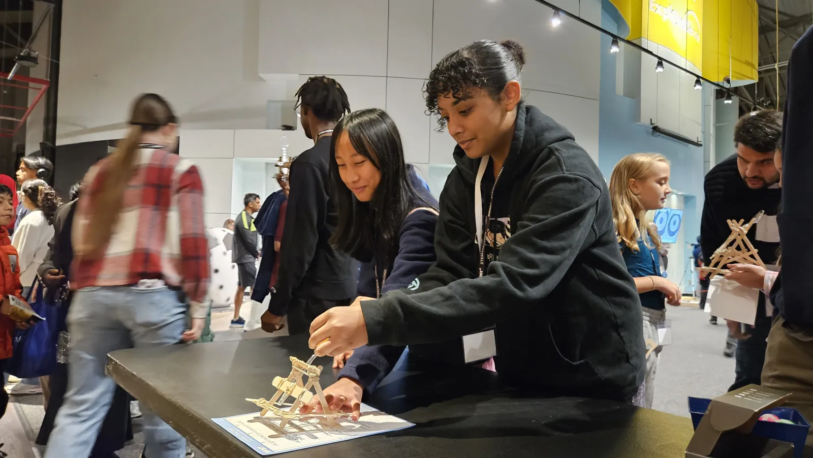 two students adjust a wooden catapult together at the testing table