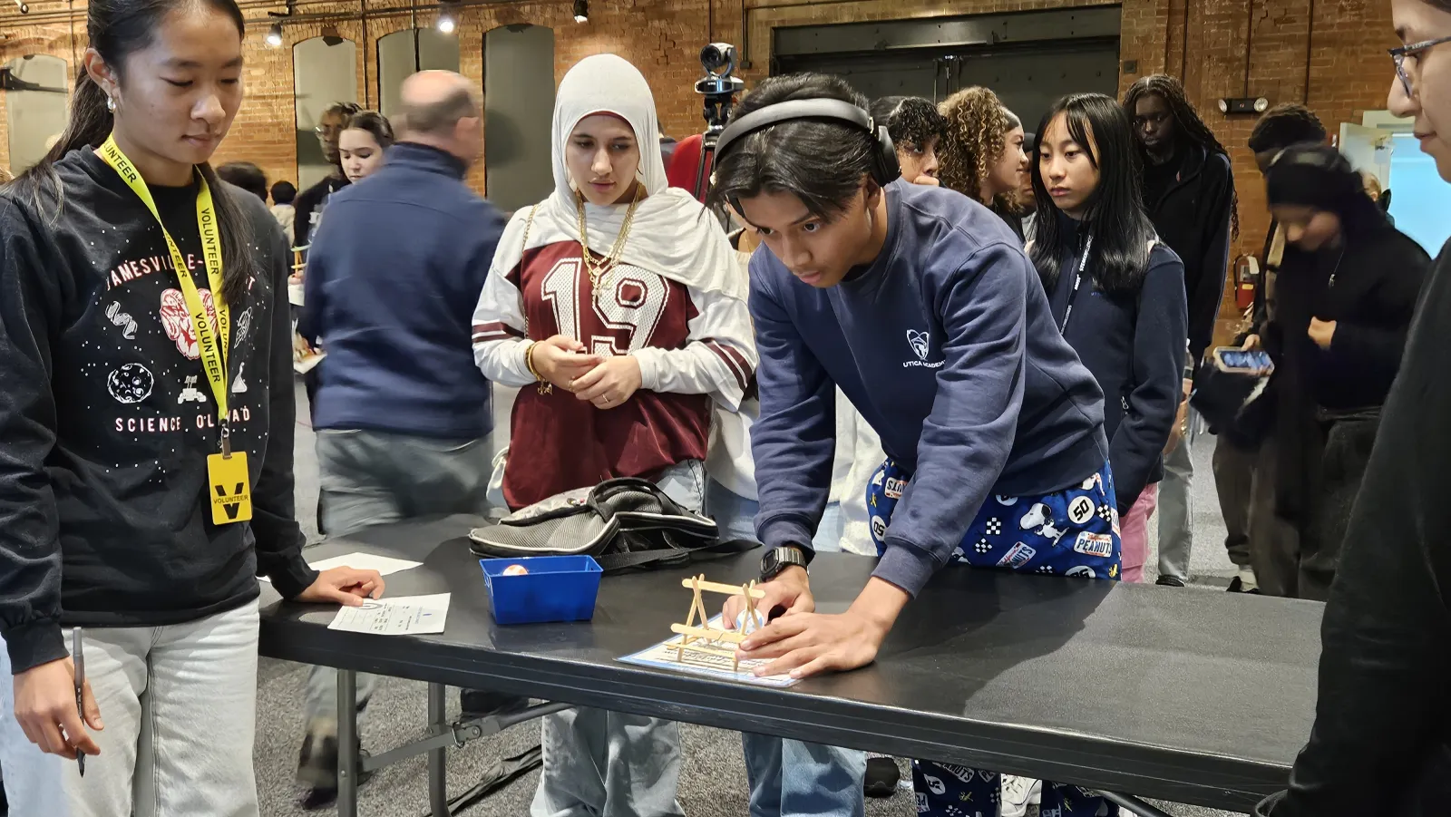 three students work together to prepare a wooden tabletop catapult