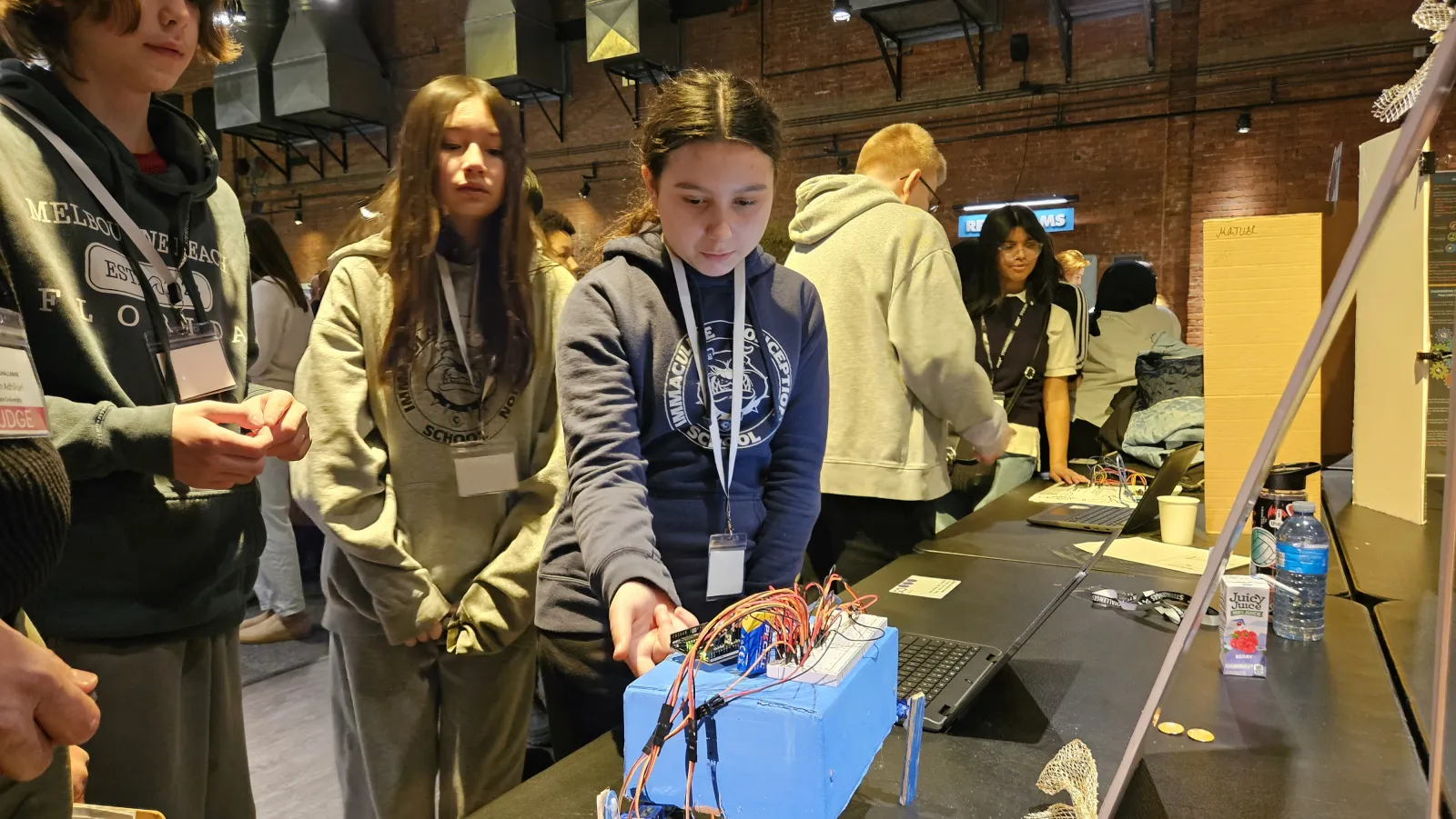 a student adjusts a wired blue robot while teammates watch closely