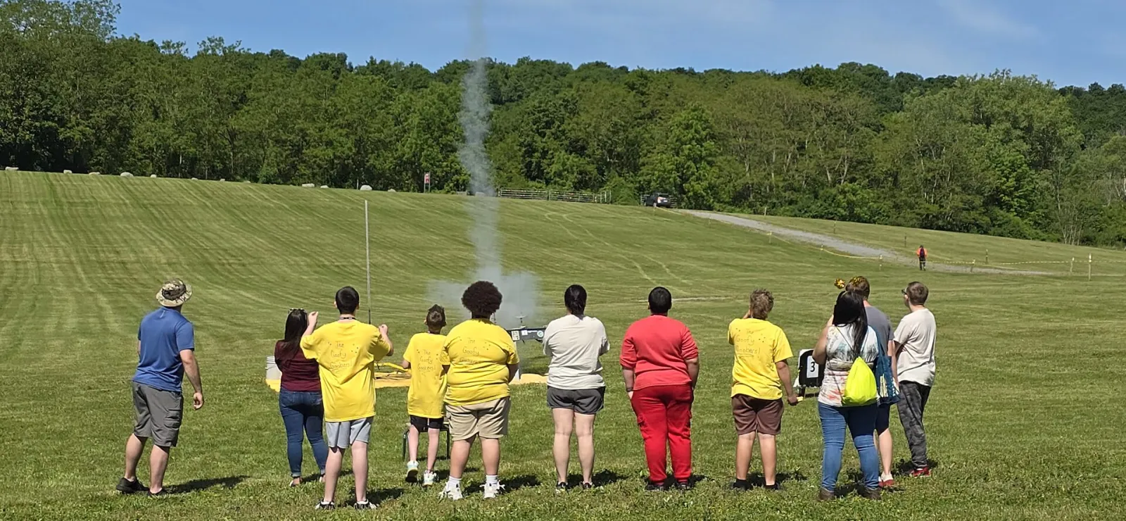 students watch a rocket’s smoke trail rise over the field
